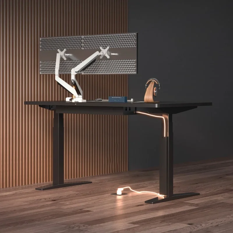 E7 Pro Line electric standing desk. Black desk with a white dual monitor arm, headphone stand and small devices in a warm wood-slat room, with a lit cable running down the leg to a floor socket.